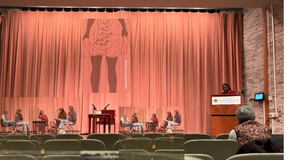 This image captures a scene in an auditorium or lecture hall, likely during an event or presentation. The overall impression is one of a staged discussion or artistic performance. In the background, a large,